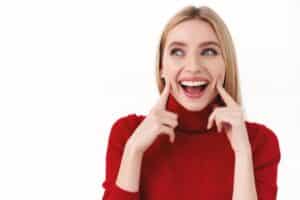 a lady is pointing towerds her teeth with a smile